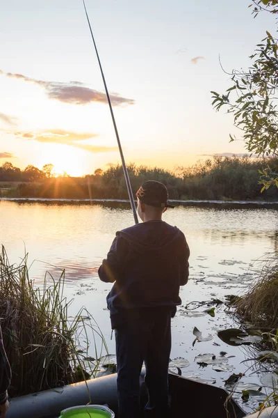 Jongen visser vangt vis op de oever van de vijver bij dageraad. — Stockfoto