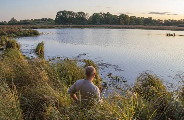 En fiskare fångar fisk vid dammens strand i gryningen. — Stockfoto