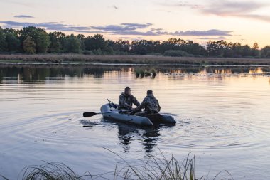 Teknedeki avcılar yaban ördeklerini aramak için gölette yüzerler.