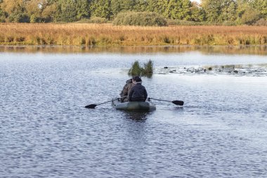 Teknedeki avcılar yaban ördeklerini aramak için gölette yüzerler.