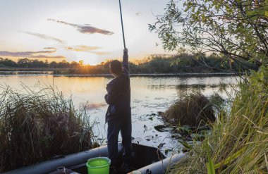 Çocuk balıkçı şafak vakti göletin kıyısında balık yakalar..