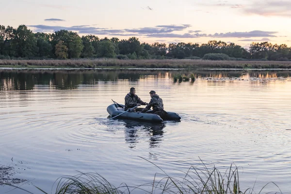 Vadászok egy csónakban úsznak egy tóban vadkacsák után kutatva. — Stock Fotó