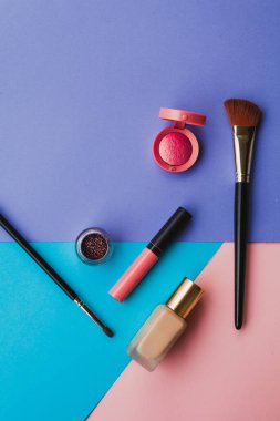 Modaya ait parlak ojeler ve dekoratif kozmetik ürünleri mavi, mor ve pembe arka planda. Asgari düzeyde. Uzayı kopyala Güzellik blogcusu kavramı. Üst görünüm.