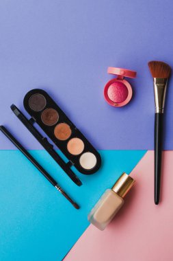 Modaya ait parlak ojeler ve dekoratif kozmetik ürünleri mavi, mor ve pembe arka planda. Asgari düzeyde. Uzayı kopyala Güzellik blogcusu kavramı. Üst görünüm.