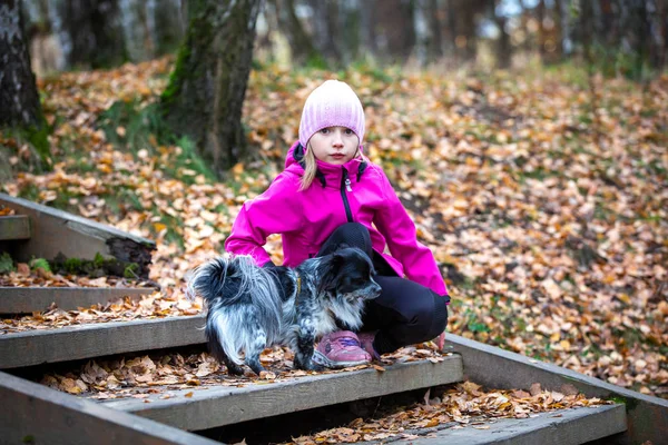 A girl of Caucasian appearance holds in her hands a small dog.  Walk in the park.