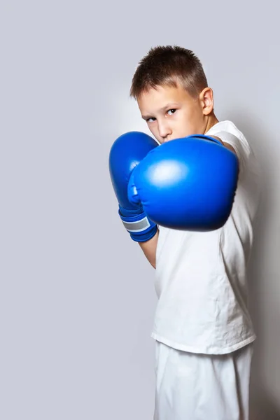 Teenager in a white T-shirt and boxing gloves on a gray background. Boxing lesson.