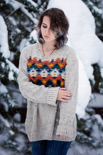 Uma menina de aparência caucasiana em uma camisola e jeans em um fundo de árvores nevadas. Dia de inverno nevado. Um passeio divertido . — Fotografia de Stock
