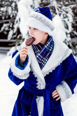 Noel Baba kostümü giymiş bir çocuk dondurma yiyor. Komik atış. Kış. Rus Noel karakteri Noel Baba. Yeni Yıl.