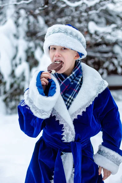 Мальчик в костюме Санта Клауса ест мороженое. Смешной выстрел. Зима. Русский рождественский персонаж Санта Клаус. Новый год . — стоковое фото