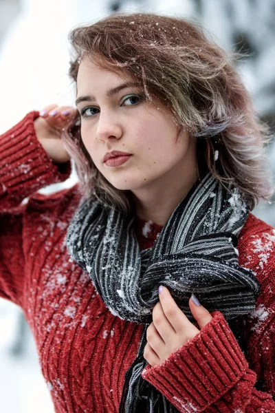 Dia de inverno. Uma linda garota de aparência caucasiana em uma camisola borgonha e cachecol na rua contra um fundo de árvores nevadas . — Fotografia de Stock