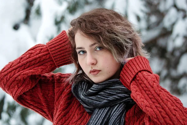 Dia de inverno. Uma menina bonita de aparência caucasiana em uma camisola borgonha e cachecol na rua contra um fundo de árvores nevadas. Inverno . — Fotografia de Stock