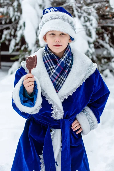 Мальчик в костюме Санта Клауса ест мороженое в заснеженном лесу. Смешной выстрел. Зима. Русский рождественский герой Дед Мороз. Новый год . — стоковое фото