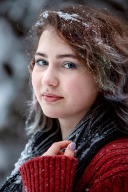 Kış günü. Kafkas görünümlü, bordo süveter ve eşarp giymiş güzel bir kız sokakta karlı ağaçların arkasında. 