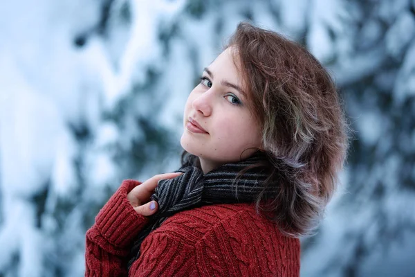 Dia de inverno. Uma linda garota de aparência caucasiana em uma camisola borgonha e cachecol na rua contra um fundo de árvores nevadas . — Fotografia de Stock