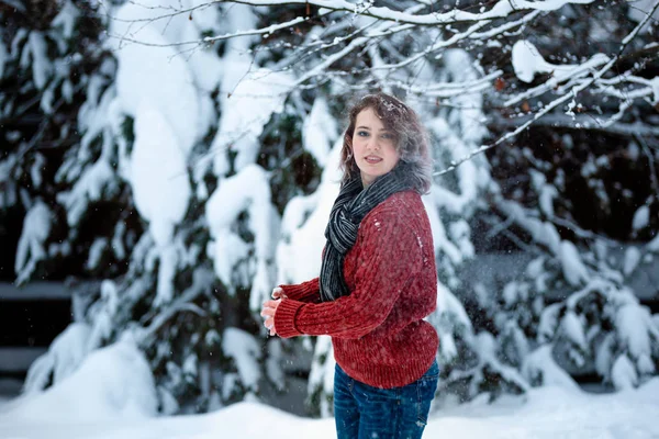 Uma linda garota de aparência caucasiana em uma camisola borgonha joga neve. Jogos de exterior. Dia de inverno . — Fotografia de Stock