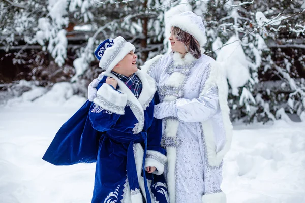 Father Frost e Snow Maiden em um fundo de árvores nevadas. Um rapaz de fato do Father Frost. Menina com o traje da Donzela da Neve. Emoção brilhante de Alegria . — Fotografia de Stock