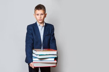 Mavi takım elbiseli, gri arka planda büyük kitapları olan genç bir çocuk. Kavram: öğrenmenin karmaşıklığı, yeni şeyler öğrenmenin.