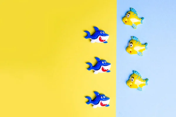 Пластиковая рыба и акула на синем и желтом фоне. Смешные детские игрушки из полимерной глины, плоско, копировальное пространство . — стоковое фото