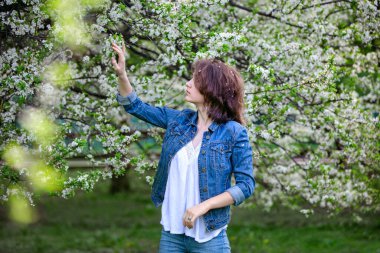 Çiçek açan ağaçların arka planında Avrupalı görünümlü güzel bir kız. Güneşli bir bahar günü. Saçında çiçek yaprakları.