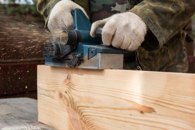 Elektrikli planörü olan bir katılımcının elleri. Uçan talaşlar, ahşap tahta. Bir profesyonelin işi. Ahşap.