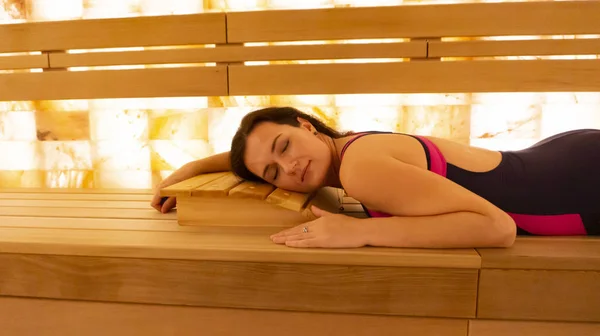 Young woman is relaxing in a warm sauna with Himalayan salt, lying on a wooden bench with her eyes closed