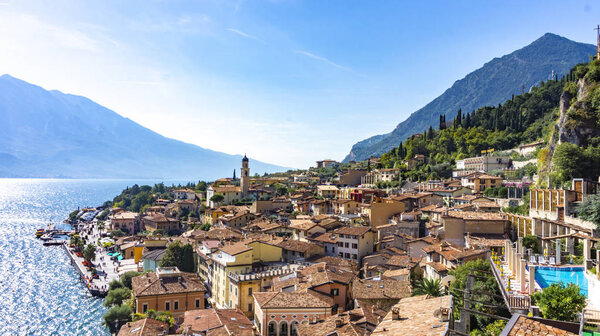 Postcard scenic panoramic view of the old European town on the shore of a mountain lake. City of Limone sul Garda aerial view. Tiled roofs of a medieval town in the Alps