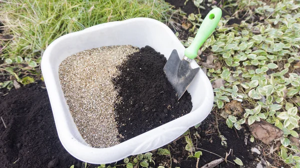 Preparation of soil mixture from fertile compost, humus and vermiculite in a white container in the garden. Mixing the soil components for the preparation of the substrate for transplanting plants.