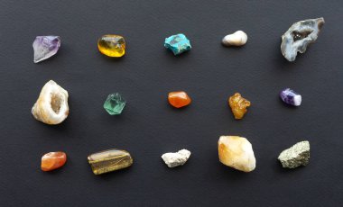Siyah bir zemin üzerinde farklı jeolojik kayalardan oluşan değerli taşlar, kristaller ve mineraller. Mineral koleksiyoncuları için yarı değerli taşlar koleksiyonu. Sihirli özellikleri olan iyileştirici mücevherler.
