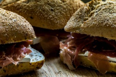 Tahta bir tahtanın üzerinde üç serrano jambonlu sandviç ve kepekli ekmek ve peynirli ekmek kırıntıları.