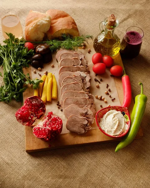 boiled beef tongue on a wooden board with fresh herbs, vegetables, bread and spices