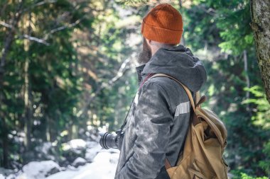 A man with a beard is standing in the woods with a camera. Conceptual design.