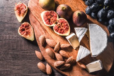 Tahta bir arka planda üzüm, incir ve fındık ile servis edilen peynir tabağı..