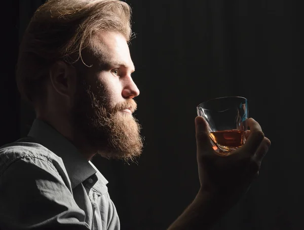 Retrato de um jovem bonito com barba bebendo álcool de um copo . — Fotografia de Stock