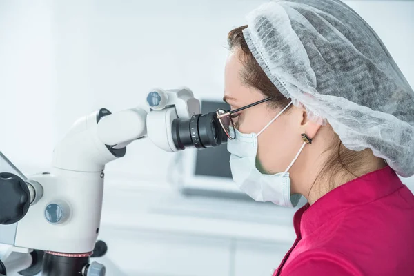 Крупный план врача-дантиста, смотрящего в микроскоп в стоматологическом кабинете — стоковое фото