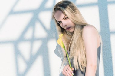 Tarz sahibi, güzel sarışın bir kız elinde çiçekle, geometrik bir desenin arka planında.