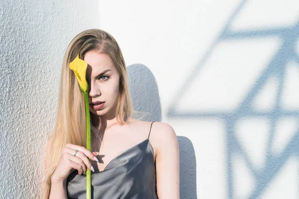 Menina loira elegante, bonita com uma flor em suas mãos, contra o fundo de um padrão geométrico — Fotografia de Stock