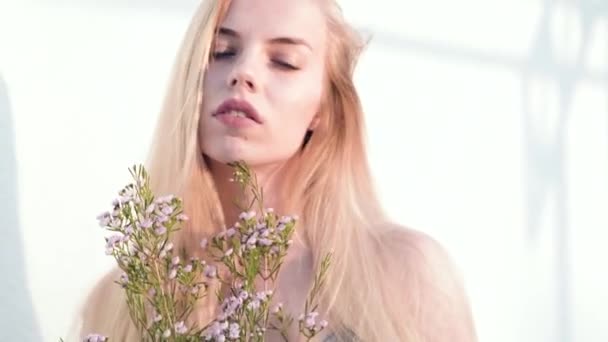 Snygg, vacker blond flicka med en blomma i händerna, mot bakgrund av ett geometriskt mönster — Stockvideo