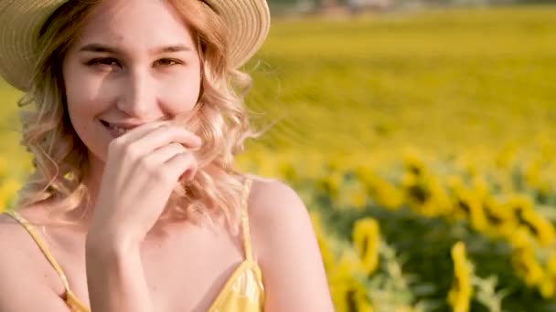 Κοντινό πλάνο πορτρέτο του όμορφου, χαρούμενου κοριτσιού με καπέλο, στέκεται σε ένα χωράφι με ηλιοτρόπια — Αρχείο Βίντεο