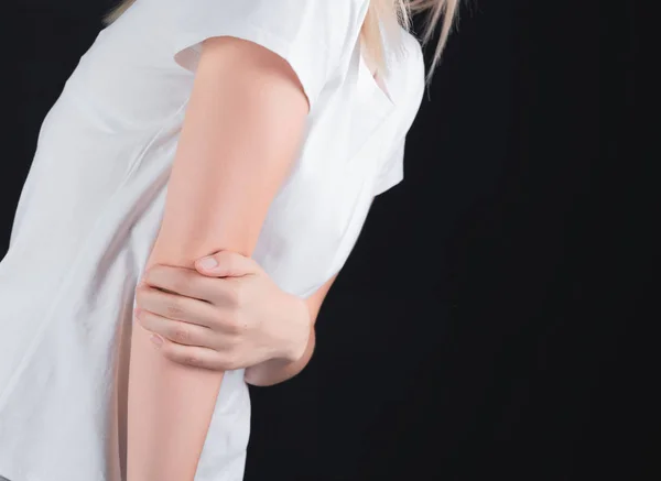 Close-up de uma menina segurando um cotovelo machucado, em um fundo preto isolado — Fotografia de Stock