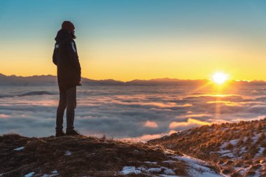 Bir adam yüksek dağlarda, gün batımında, bulutların üzerinde duruyor..