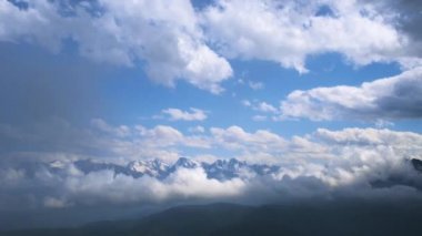 Mavi bulutlu gökyüzünün altında kar bulunan dağların kış manzarası. Hızlı hareket eden bulutların videosu