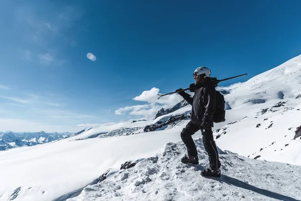 Un hombre con esquís se encuentra en lo alto de las montañas disfrutando del paisaje. Ir a esquiar cuesta abajo, relajación extrema —  Fotos de Stock