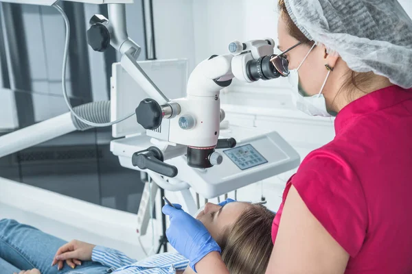 El médico dentista mira con un microscopio los dientes del paciente — Foto de Stock