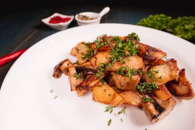 Tahta bir masada mantarlı bir tabak iştah açıcı patates, baharatların arasında. Yemek endüstrisindeki yemek fotoğrafçılığı, karanlık arka plan..