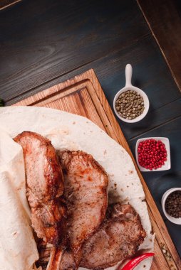 İştah açıcı kızarmış et, ahşap bir tepside, baharatların arasında yatıyor. Yemek endüstrisindeki yemek fotoğrafçılığı, karanlık arka plan.