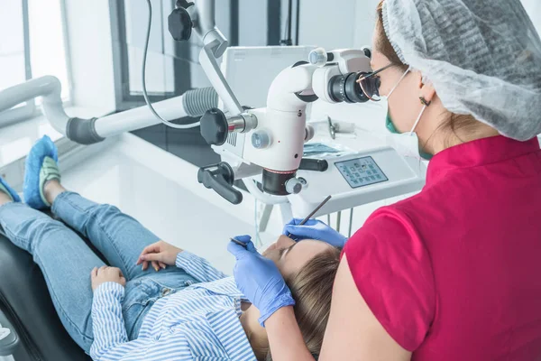 El médico dentista mira con un microscopio los dientes del paciente. El concepto de atención y tratamiento de la salud en las instalaciones médicas — Foto de Stock
