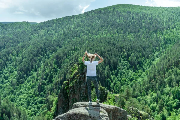 A beautiful young girl stands high in the mountains and looks at the forest — Stock Photo, Image