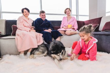 Anne, baba ve iki kız hafta sonları evde rahatlar ve köpekle oynarlar. Evde birlikte vakit geçiren ideal aile kavramı.