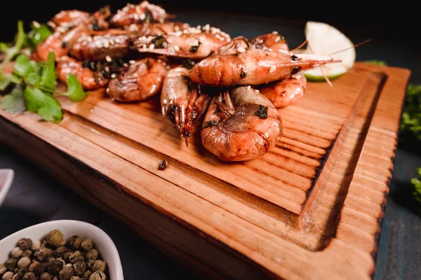 Appetitlich gebratene Garnelen auf einem hölzernen Tablett zwischen Gewürzen. Studioaufnahmen von Lebensmitteln in der Kochbranche, dunkler Hintergrund — Stockfoto