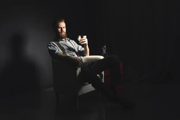 Egy töprengő, jóképű fiatalember portréja, egy pohár alkohollal a kezében, elszigetelt fekete háttérrel. A szórakozás, pihenés és kikapcsolódás fogalma — Stock Fotó